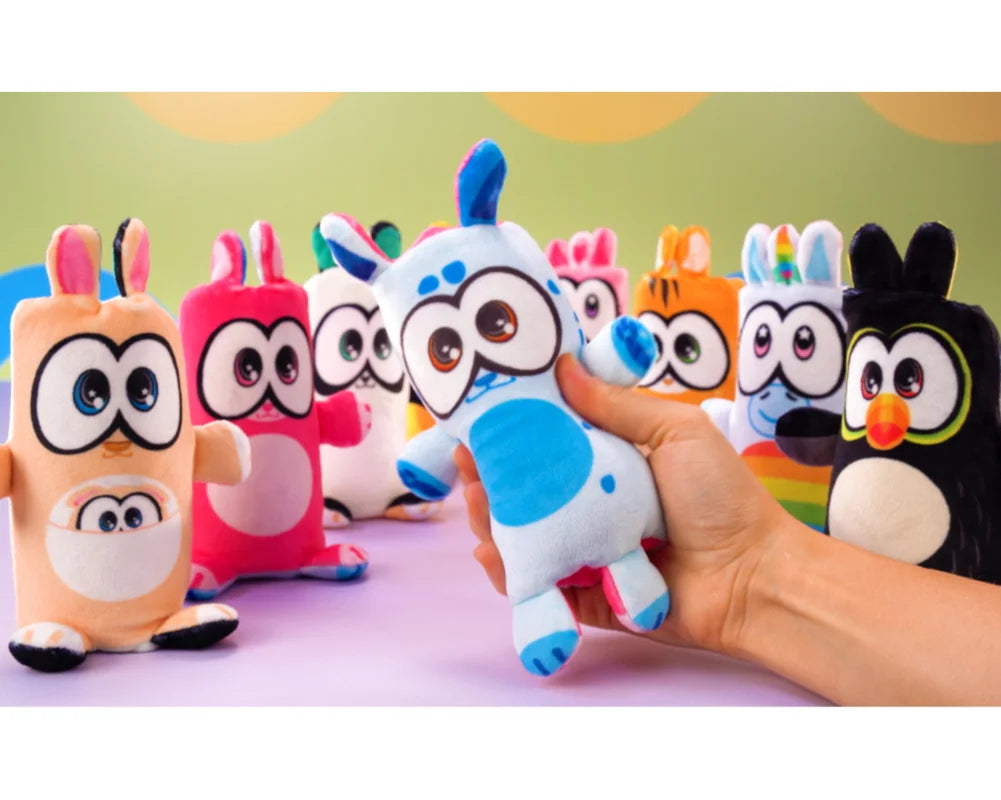 Ręka trzyma maskotkę Flipzers jednorożec na tle kolorowych pluszowych maskotek Yamann