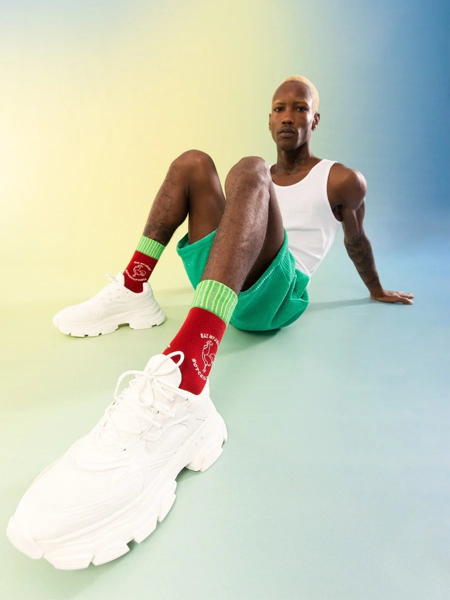 Mężczyzna w białym tank topie i zielonych szortach noszący czerwone skarpetki hot sauce z zielonym ściągaczem i białe sneakersy