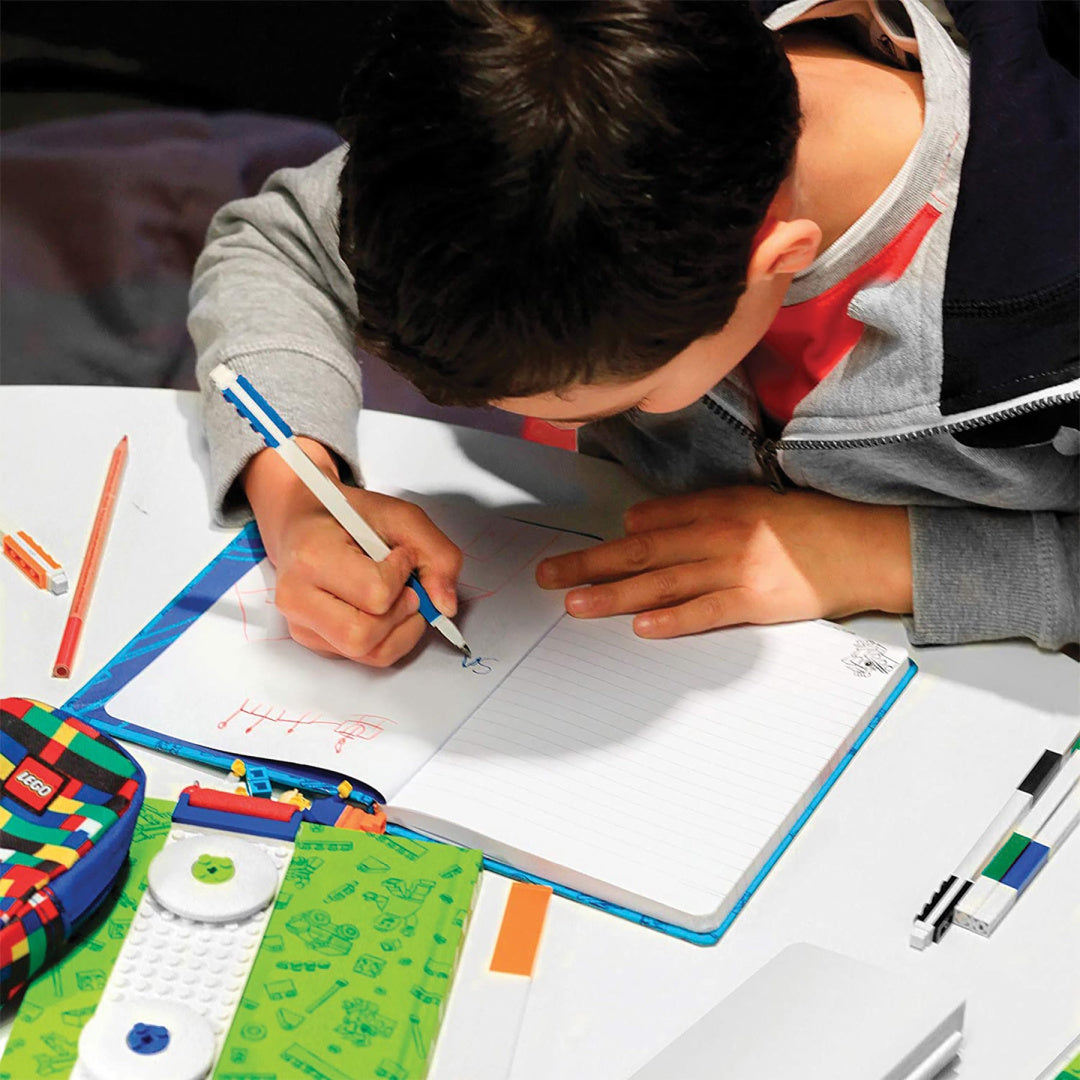 Dziecko piszące w zeszycie kolorowymi długopisami żelowymi LEGO na biurku z przyborami szkolnymi