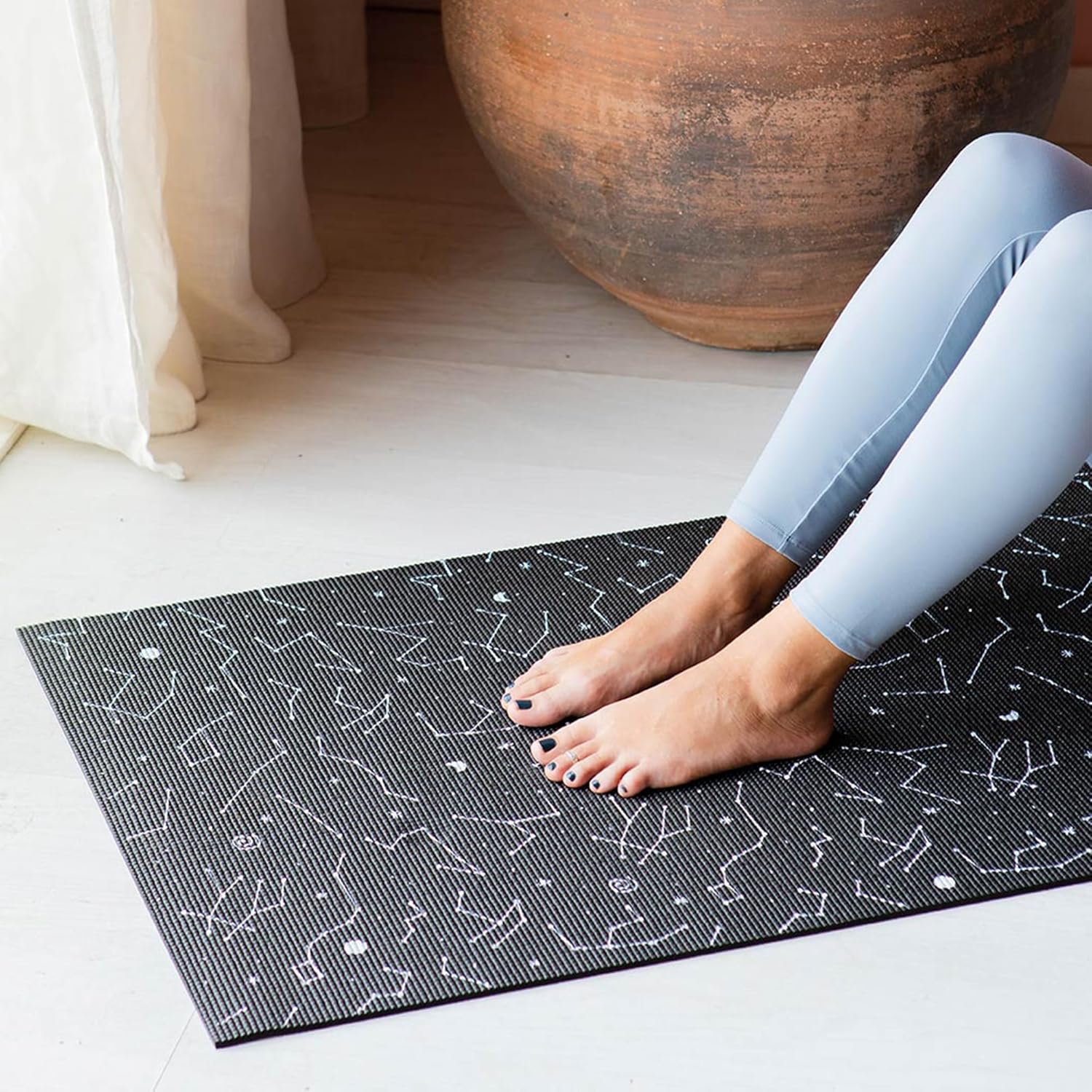 Czarna mata do jogi cosmos z wzorem gwiazdozbiorów i nogi osoby w jasnych legginsach