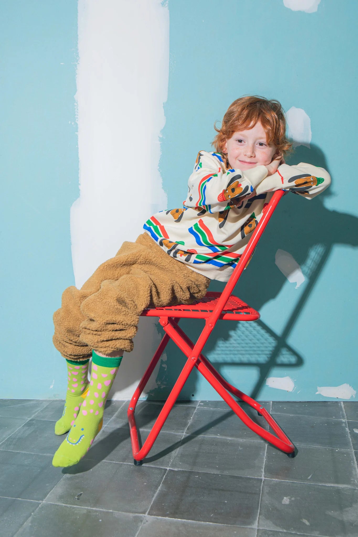 Dziecko siedzące na czerwonym krześle w kolorowych skarpetkach dziecięcych krokodyl zielonych z różowymi kropkami