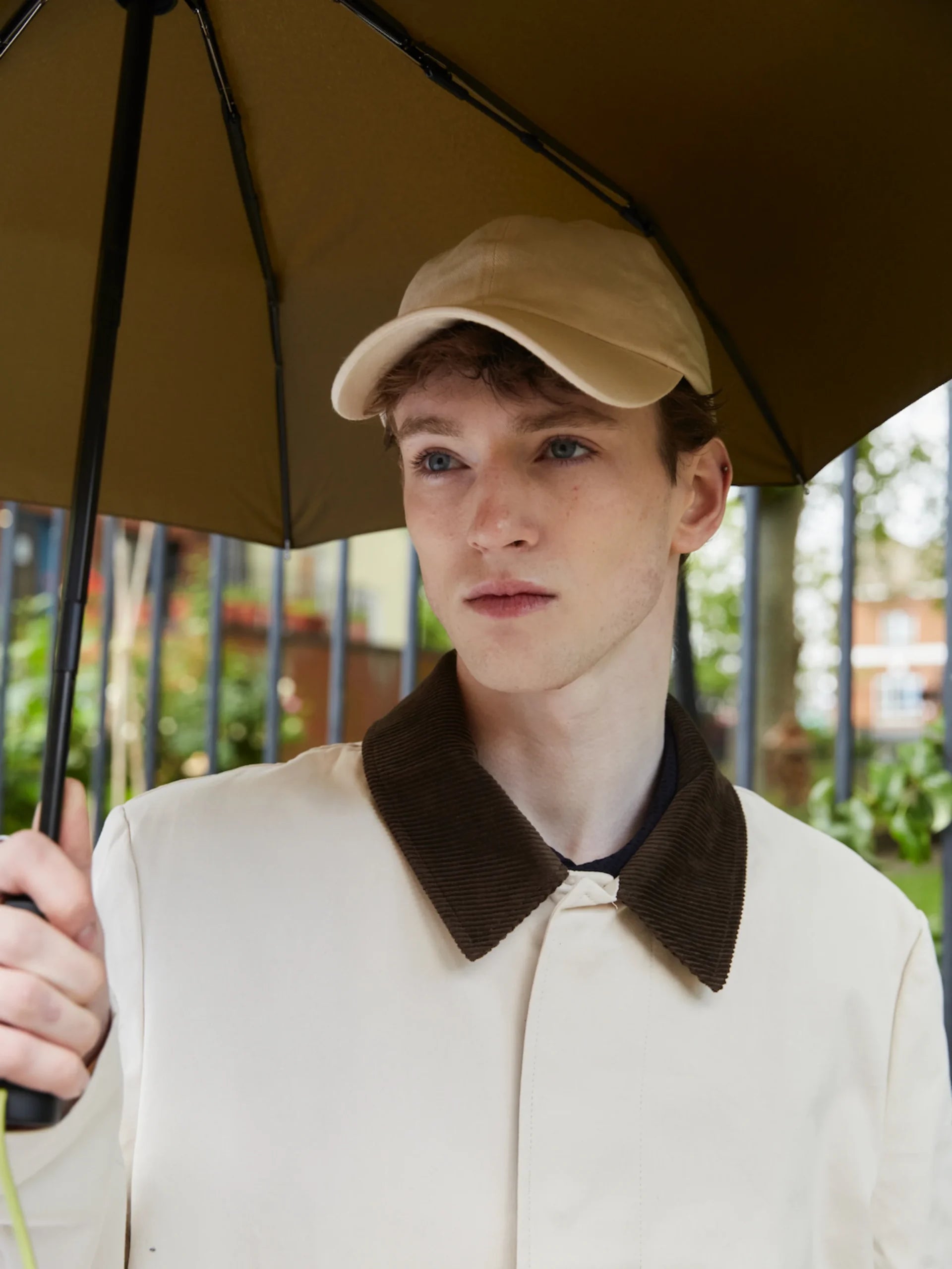 Młody mężczyzna pod trzyma parasolkę automatyczną ciemną oliwkową marki LOQI na zewnątrz