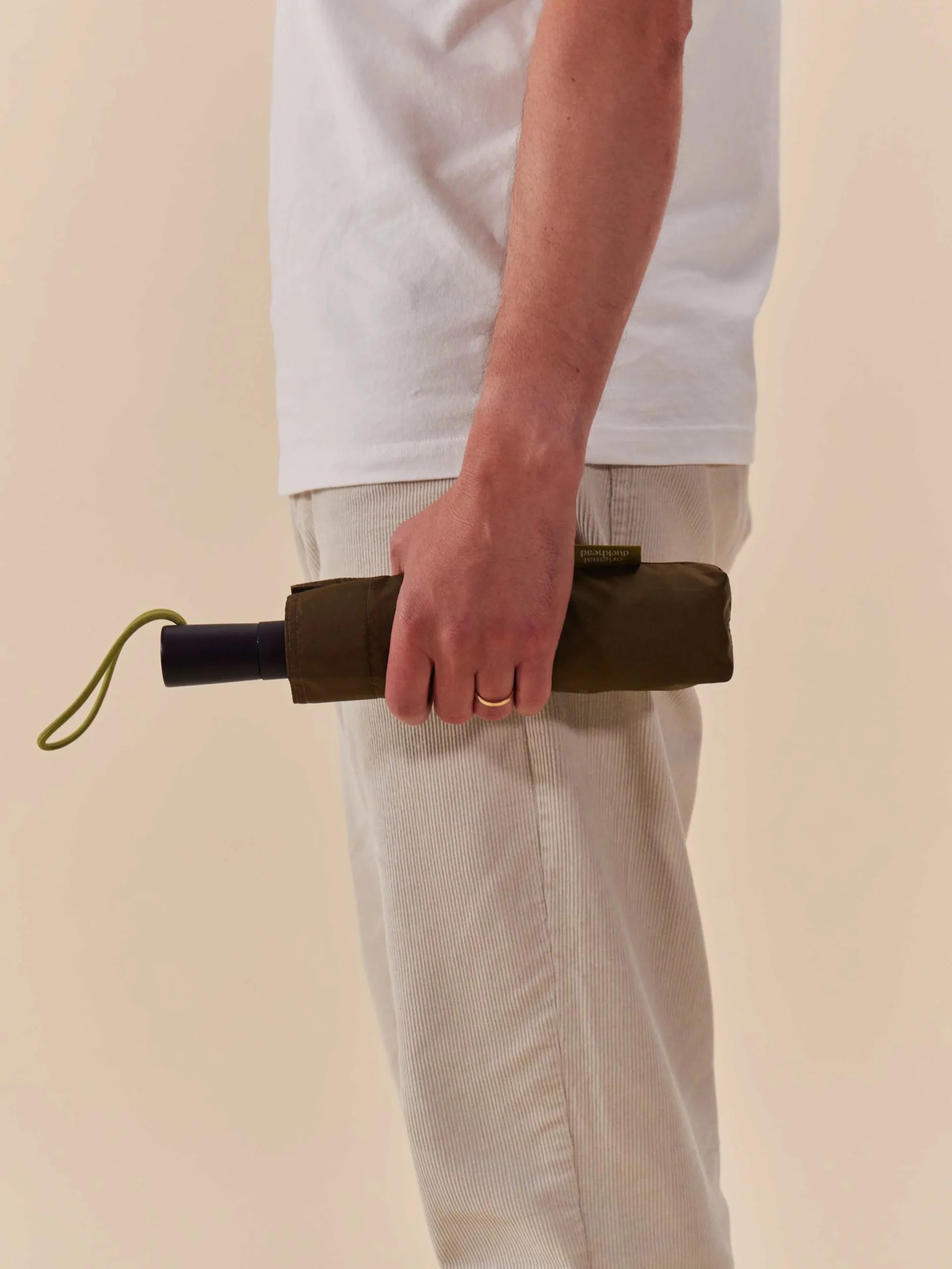 Parasolka automatyczna ciemna oliwkowa marki LOQI trzymana w dłoni obok jasnych spodni