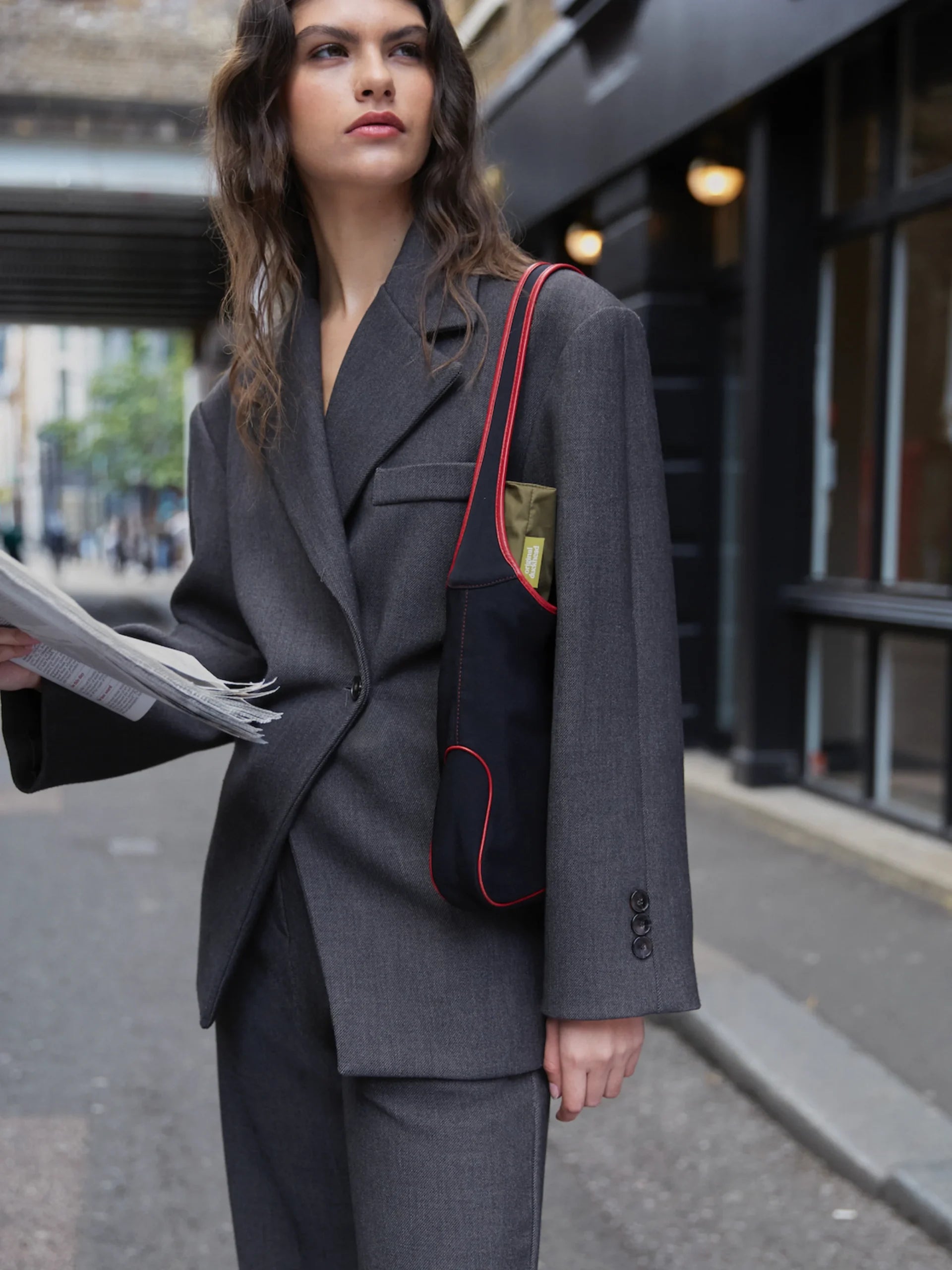 Kobieta w szarym garniturze z czarną torbą na ramię z czerwonymi detalami i parasolką automatyczną ciemną oliwkową