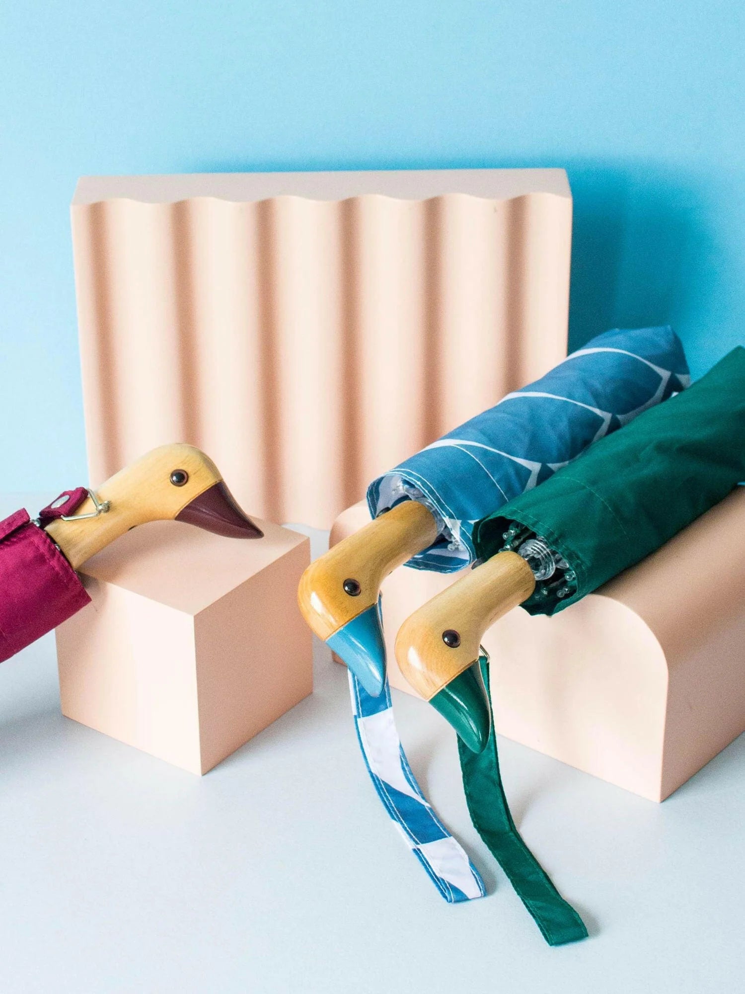 Parasolka z drewnianą rączką w kształcie kaczki w różnych kolorach na tle pastelowych kształtów