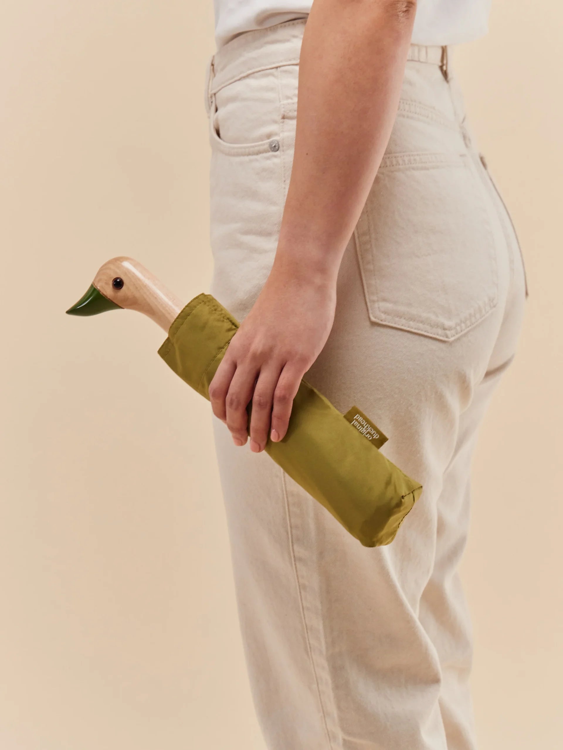 Parasolka z rączką w kształcie kaczki w zielonym pokrowcu trzymana przez osobę w jasnych spodniach