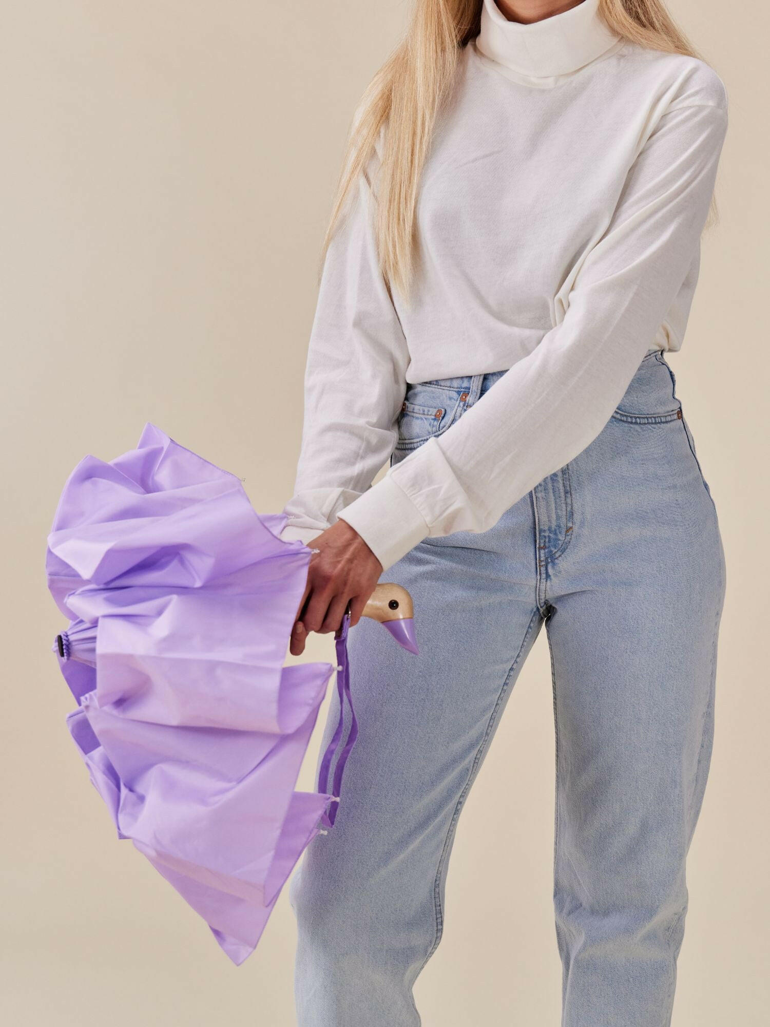 Parasolka lilak z drewnianą rączką trzymana przez kobietę w jasnej bluzce i dżinsach