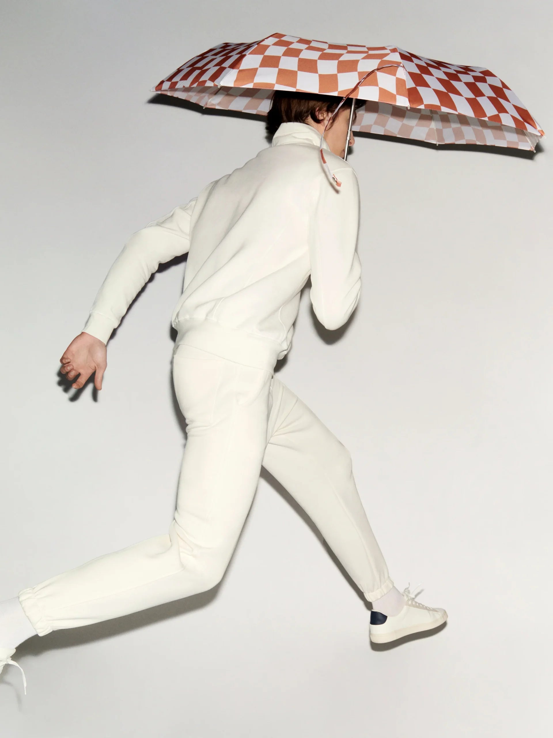 Osoba w białym ubraniu biegnąca z parasolką z rączką kaczki w biało-pomarańczową kratę