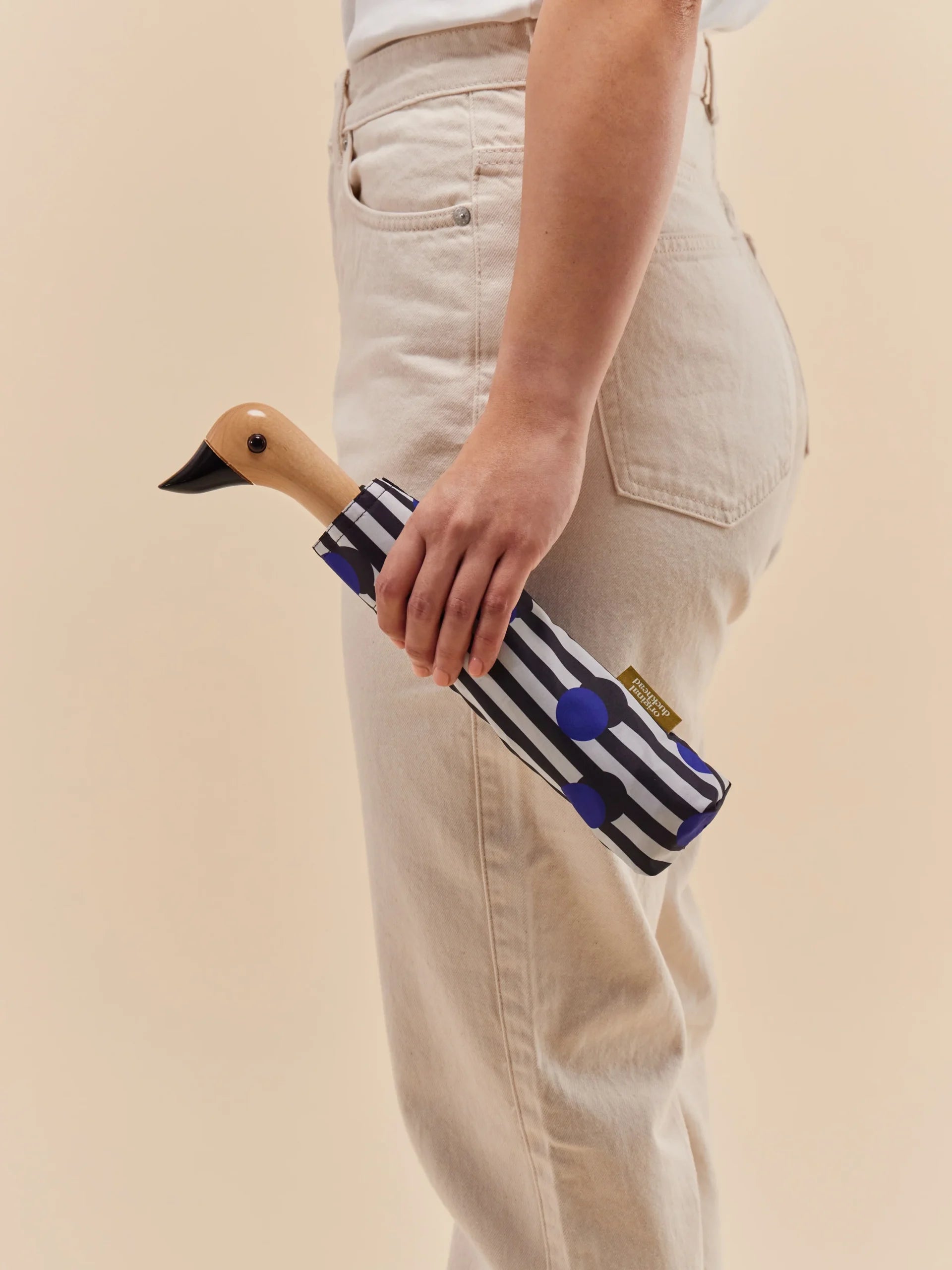 Parasolka z uchwytem w kształcie kaczki w pokrowcu w paski trzymana przez osobę w jasnych spodniach