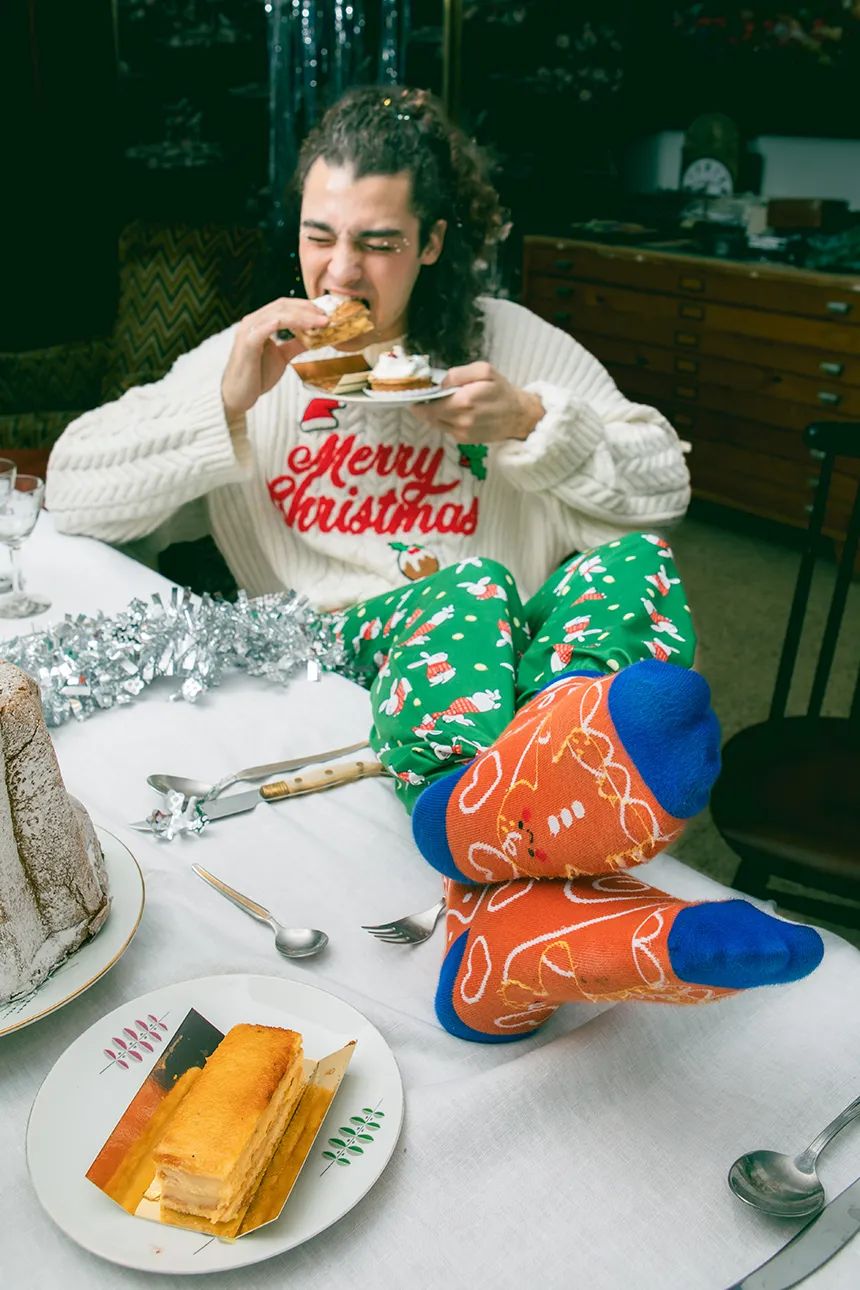 Mężczyzna w skarpetkach świąteczne ciasteczko i zielonych spodniach je ciastko przy świątecznym stole