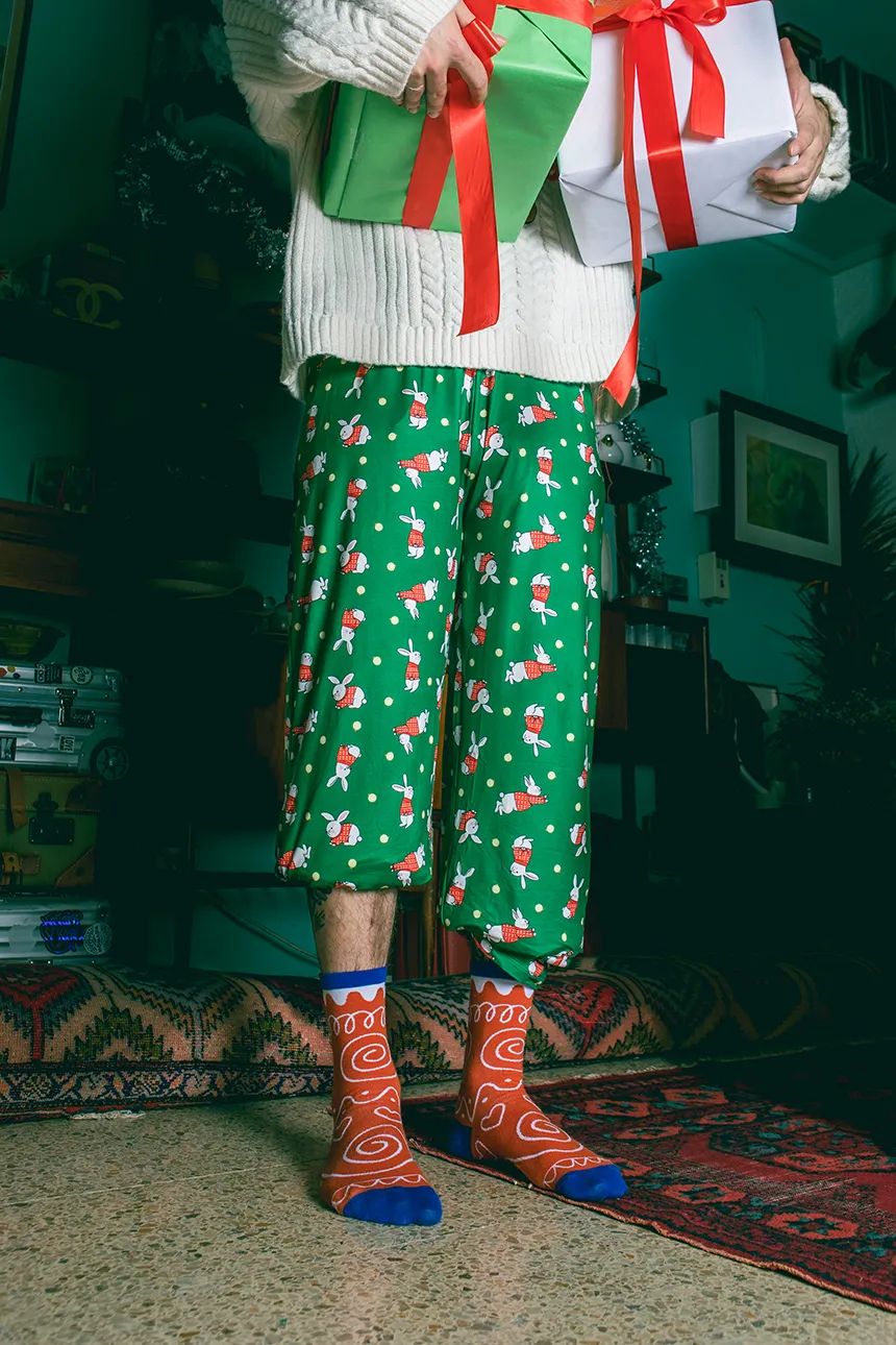 Kolorowe skarpetki świąteczne ciasteczko z czerwonym i niebieskim wzorem na stopach osoby w zielonych spodniach