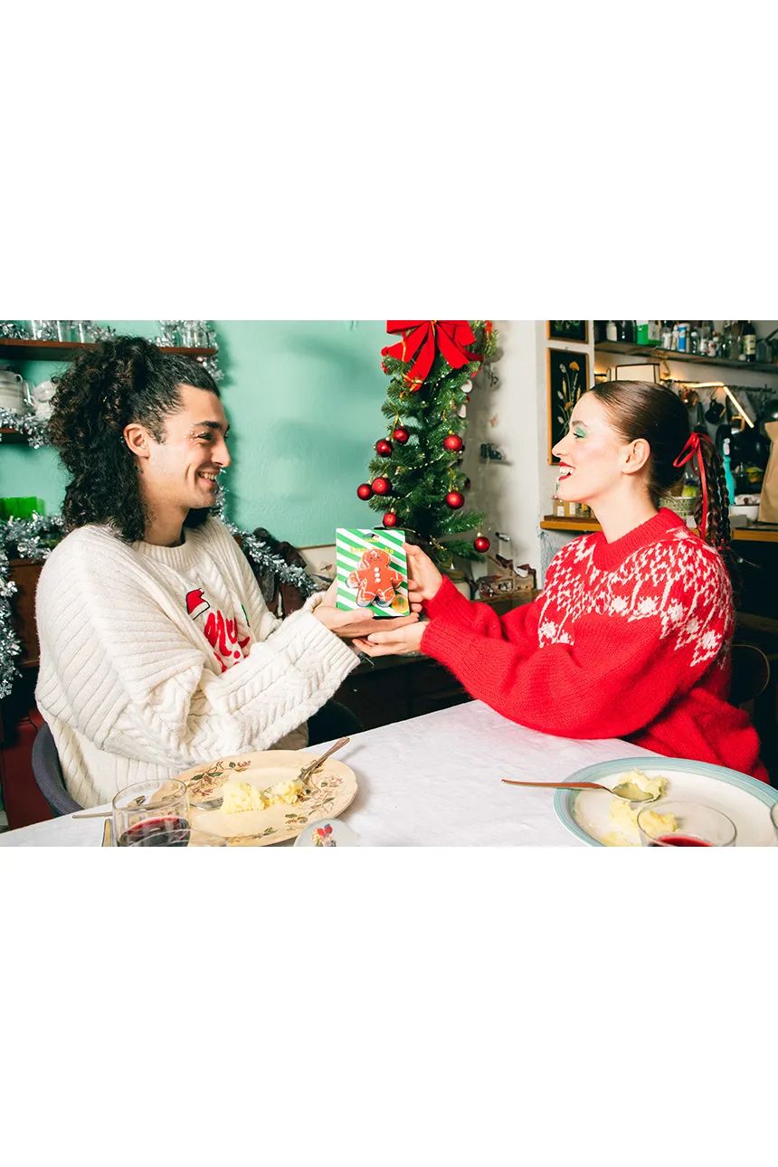 Para wymieniająca się prezentem skarpetki świąteczne ciasteczko przy udekorowanym stole w świątecznym wnętrzu