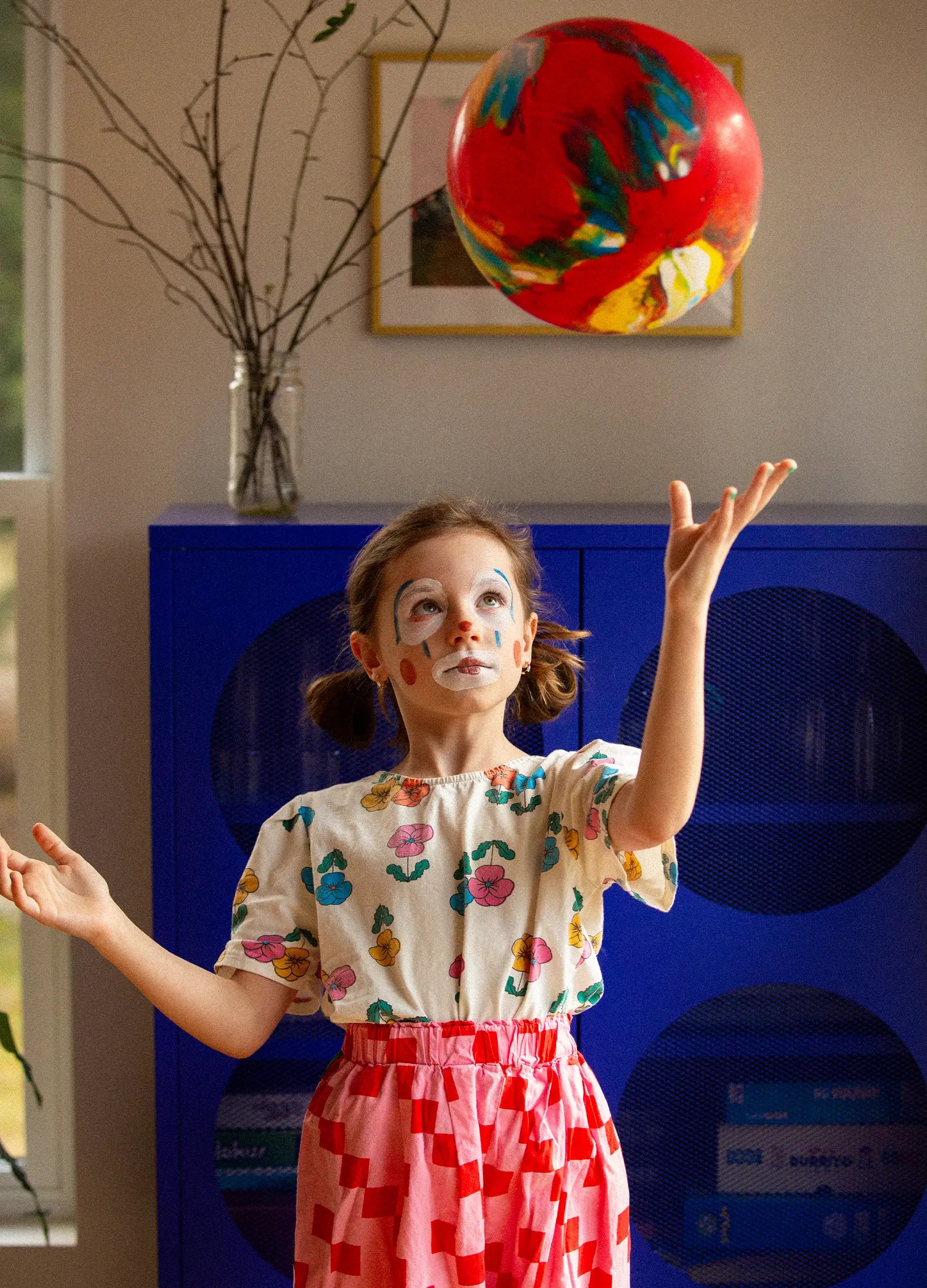 Dziewczynka z pomalowaną twarzą bawiąca się piłką w pokoju zestaw do malowania twarzy dla dzieci