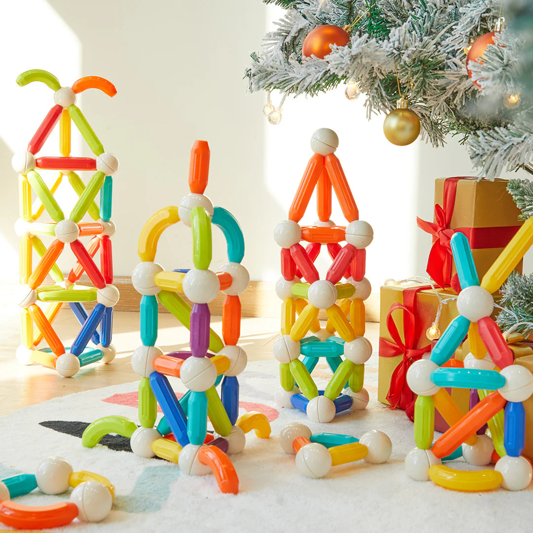 Kolorowe magnetyczne pałeczki konstrukcyjne EMS DOIY ułożone w różne wieże i kształty przy choince z prezentami