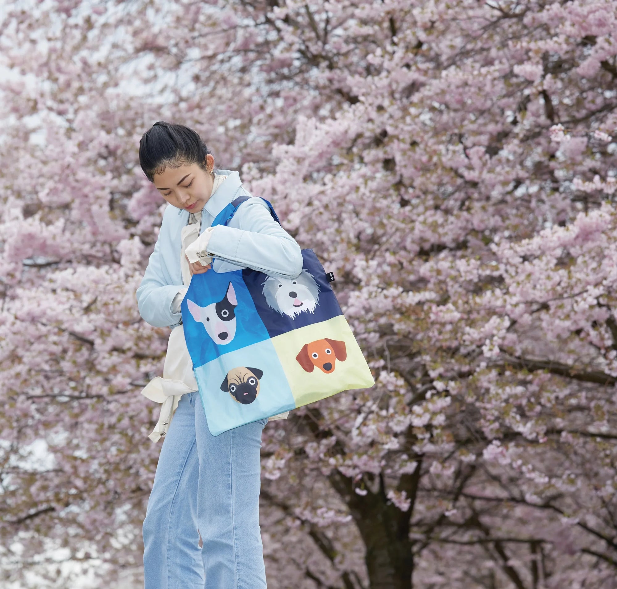 Kobieta trzyma torba podręczna z motywem psów Yamann na tle kwitnących drzew