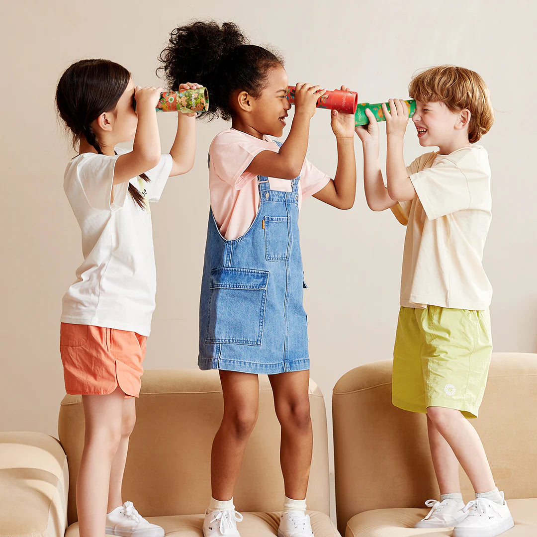 Trójka dzieci bawiących się kalejdoskopem zwierzęca olimpiada stojąc na kanapie