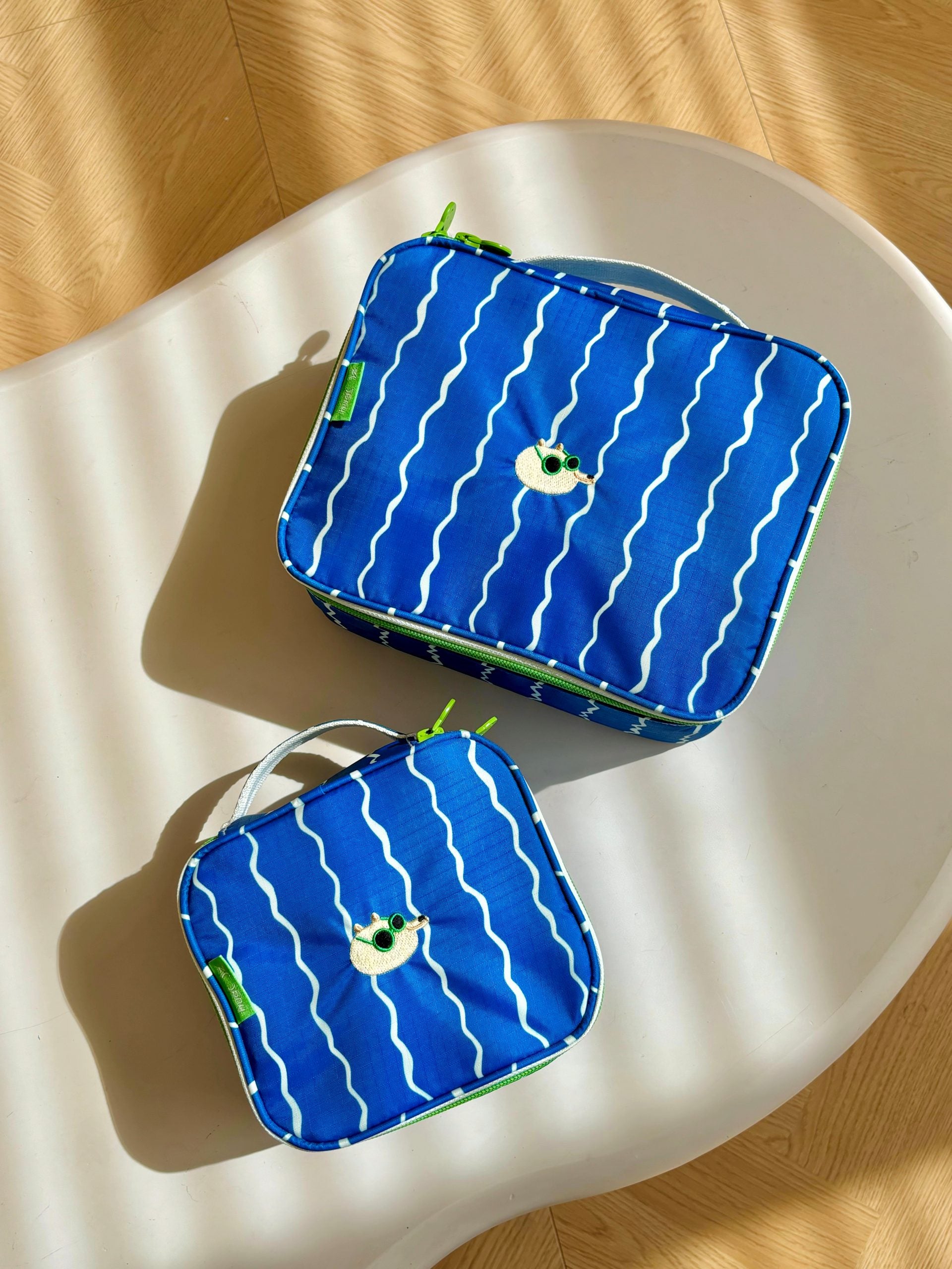 Blaue wasserdichte Reisekosmetiktasche von Yamann mit weißen wellenförmigen Mustern auf einem hellen Tisch.