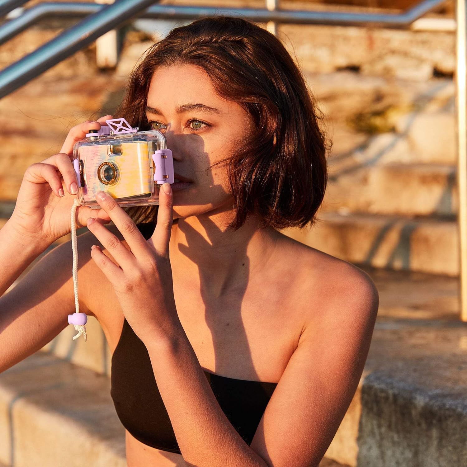 Kobieta trzymająca podwodny aparat analogowy 35 mm Sunny Life na zewnątrz przy schodach