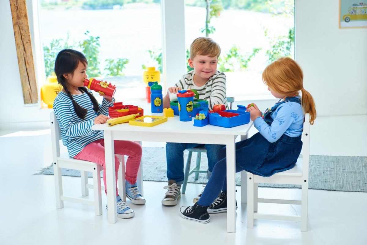 Dzieci bawiące się zabawkami LEGO z bidon LEGO dla chłopca na białym stole w jasnym pokoju