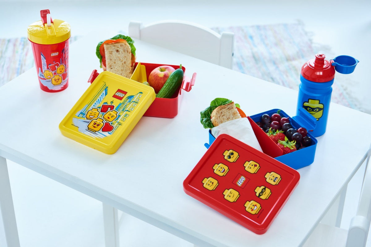 Bidon LEGO dla dzieci w kolorze czerwonym i niebieskim obok pojemników na lunch z jedzeniem na białym stole