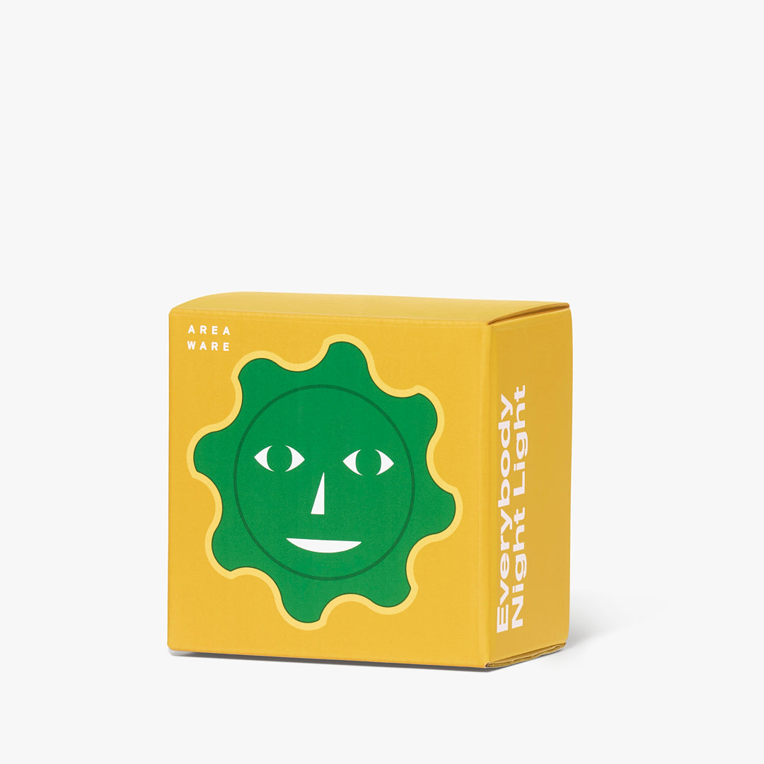 Lampka nocna dla dzieci Areaware w kształcie zielonego słoneczka na żółtym opakowaniu