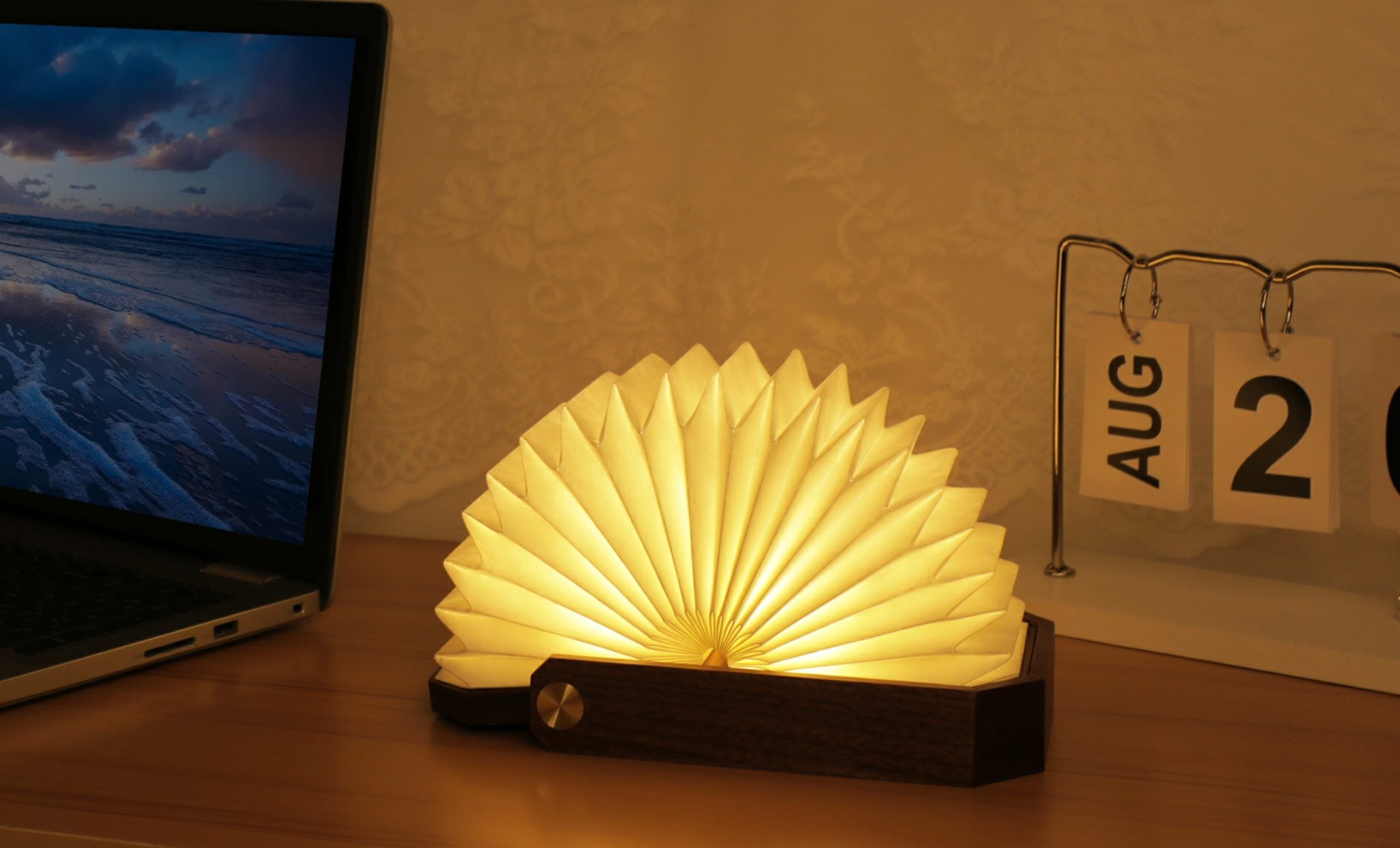 Inteligentna lampa origami orzech świecąca ciepłym światłem na drewnianym biurku obok laptopa i kalendarza