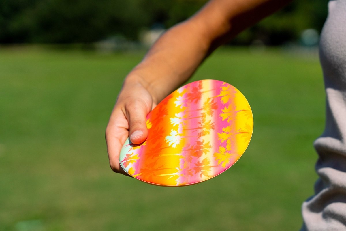 Kolorowy frisbee Waboba Wingman trzymany w ręce na tle zielonego trawnika