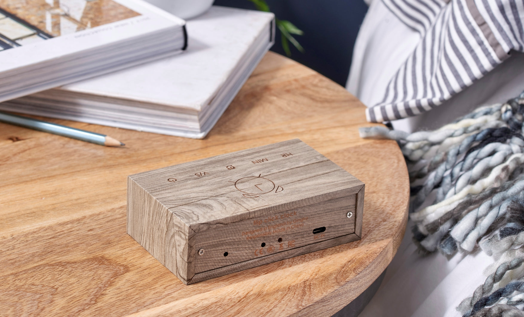 budzik flip click popiel o drewnianym wykończeniu na okrągłym drewnianym stole z książkami i kocem