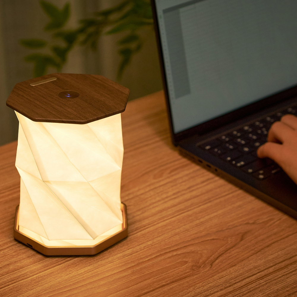 Gingko Design sześciokątna lampa stołowa z drewnianą podstawą świecąca na biurku obok laptopa