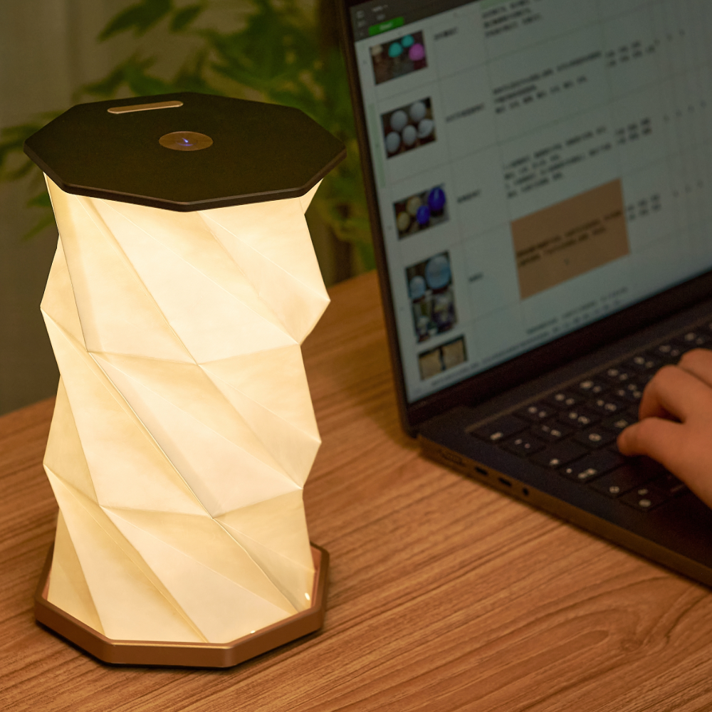 Gingko Design sześciokątna lampa stołowa o nowoczesnym geometrycznym kształcie na drewnianym biurku obok laptopa