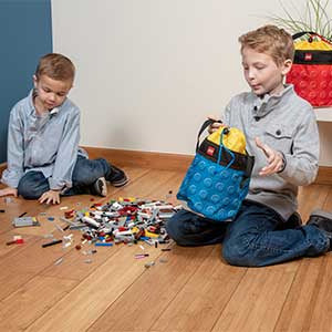 Dzieci bawiące się klockami LEGO i trzymające kubełek LEGO czerwony na drewnianej podłodze