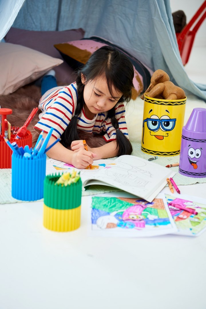 Dziecko rysujące przy stole obok zielonego pojemnika na kredki Crayola zielony i kolorowych rysunków