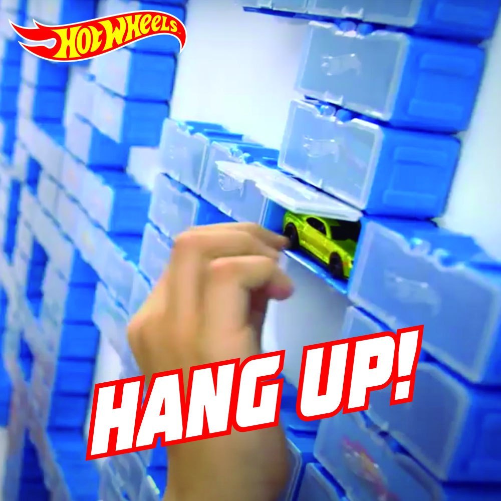 Ręka wkłada zielony samochodzik do modułowej walizki Hot Wheels z niebieskimi przegródkami