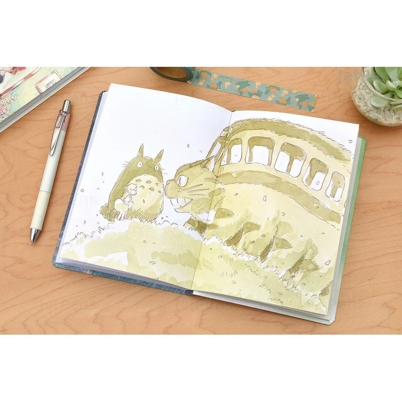 Notatnik Mój sąsiad Totoro z ilustracją z kreskówki otwarty na drewnianym biurku obok długopisu