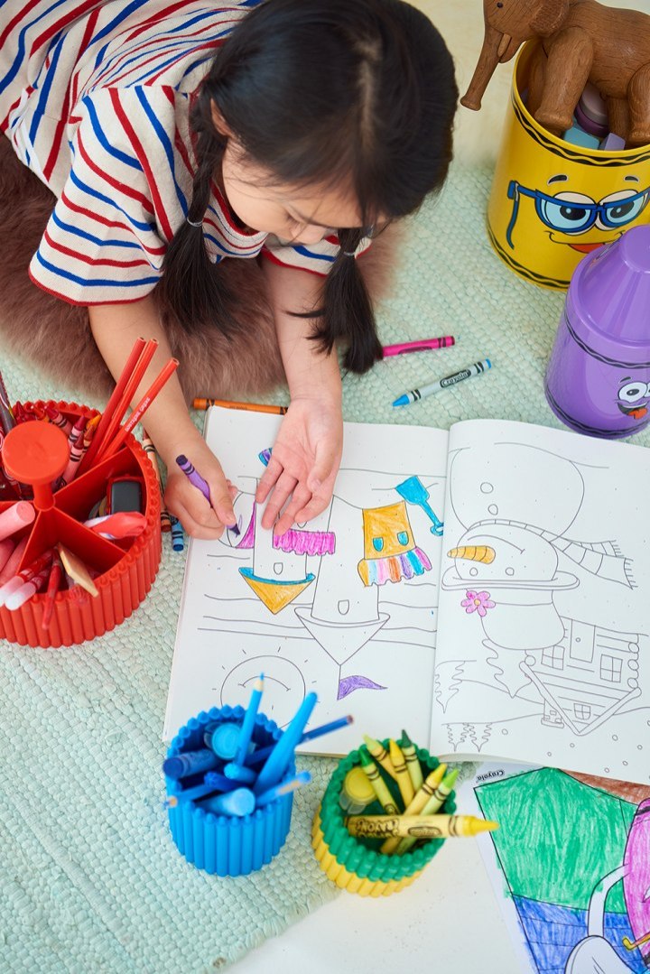 Czerwony organizer na biurko Crayola z przyborami do rysowania obok dziecka kolorującego obrazek