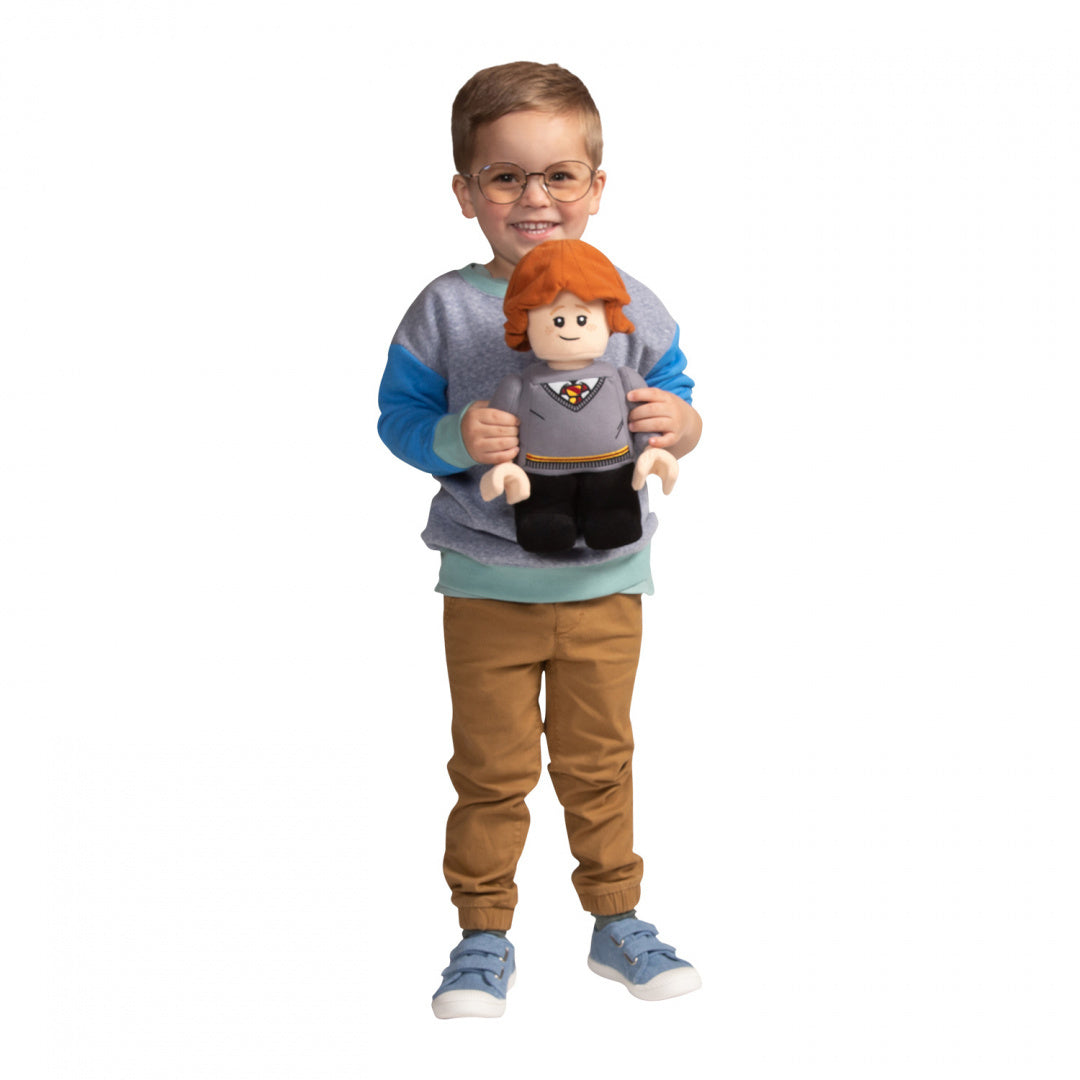 Chłopiec trzyma pluszaka Ron Weasley LEGO w szarej bluzie i brązowych spodniach na białym tle