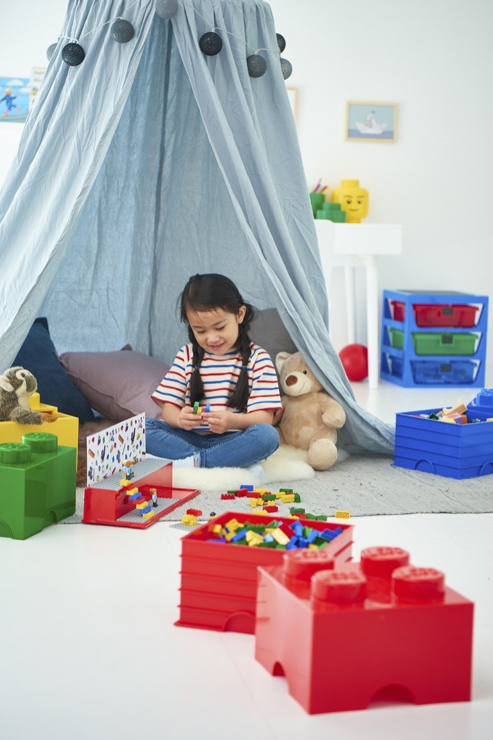 Pojemnik LEGO na zabawki w kształcie klocka z kolorowymi klockami LEGO na tle pokoju dziecięcego