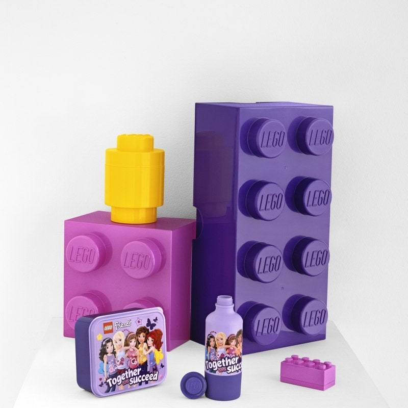 minipudełko LEGO różowe z motywem LEGO Friends na tle dużych fioletowych i żółtych klocków LEGO