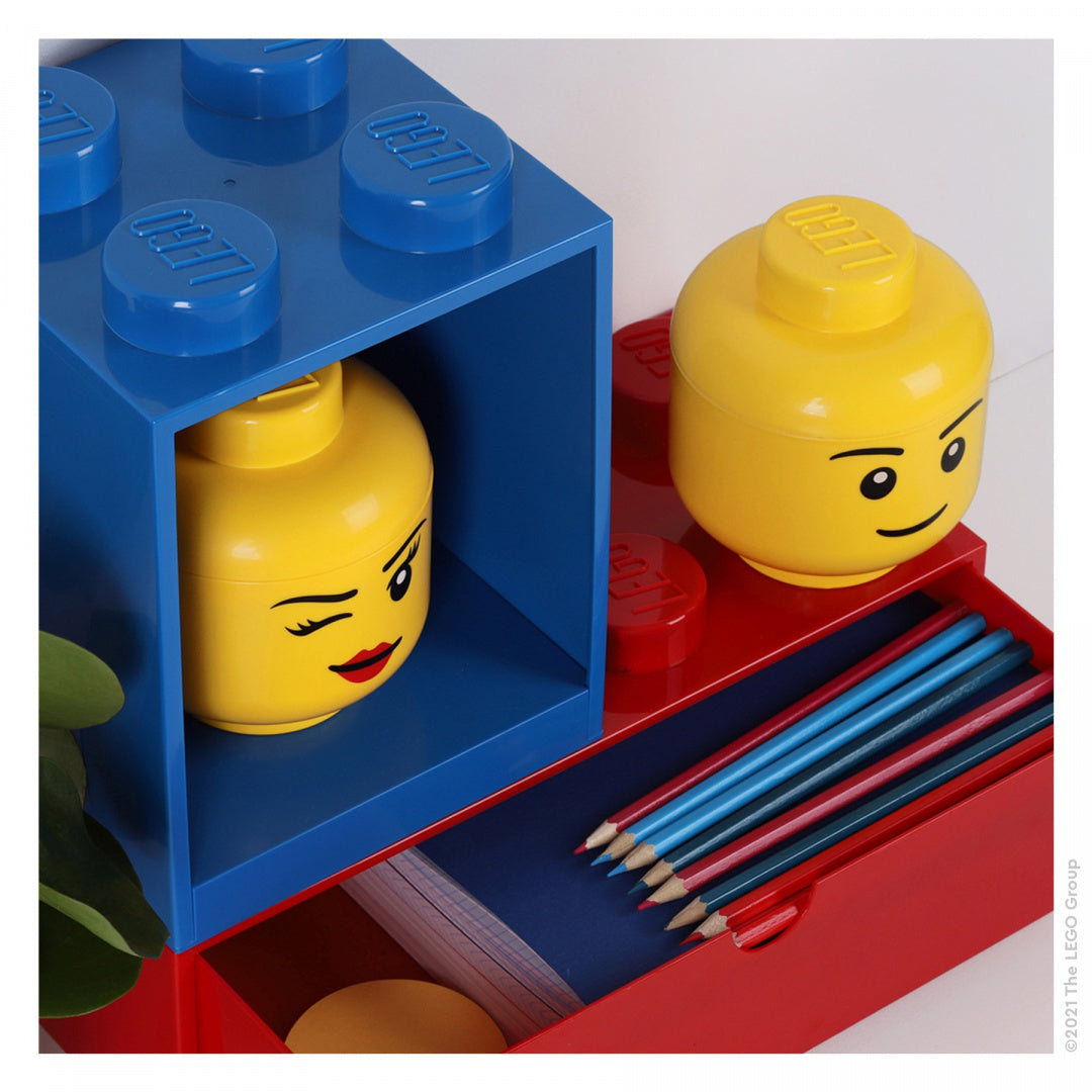 Niebieska półka LEGO Brick 4 z żółtą głową ludzika i kolorowymi kredkami na czerwonej podstawce