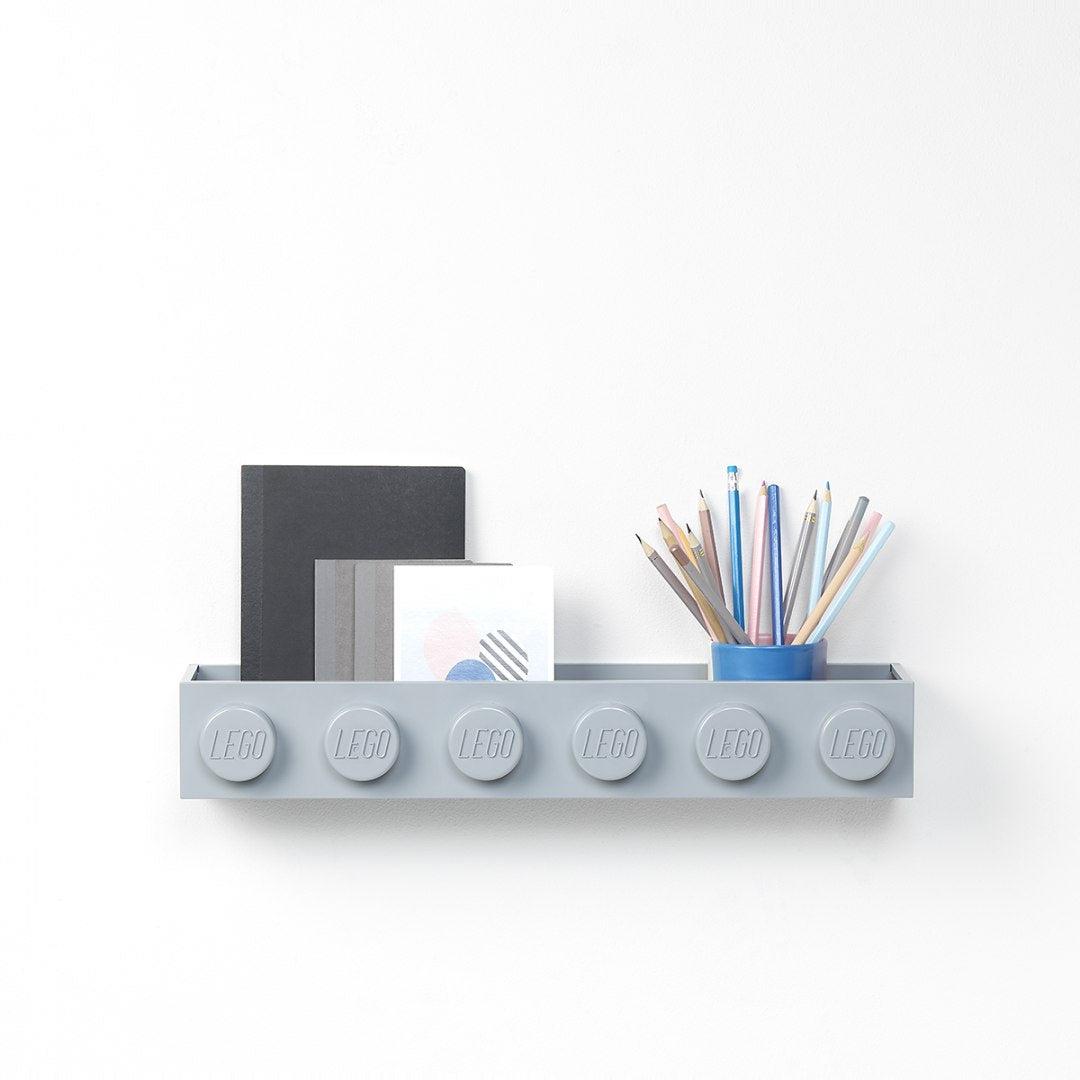 Szara półka LEGO na ścianę z dużymi kołkami przechowująca książki i przybory do pisania