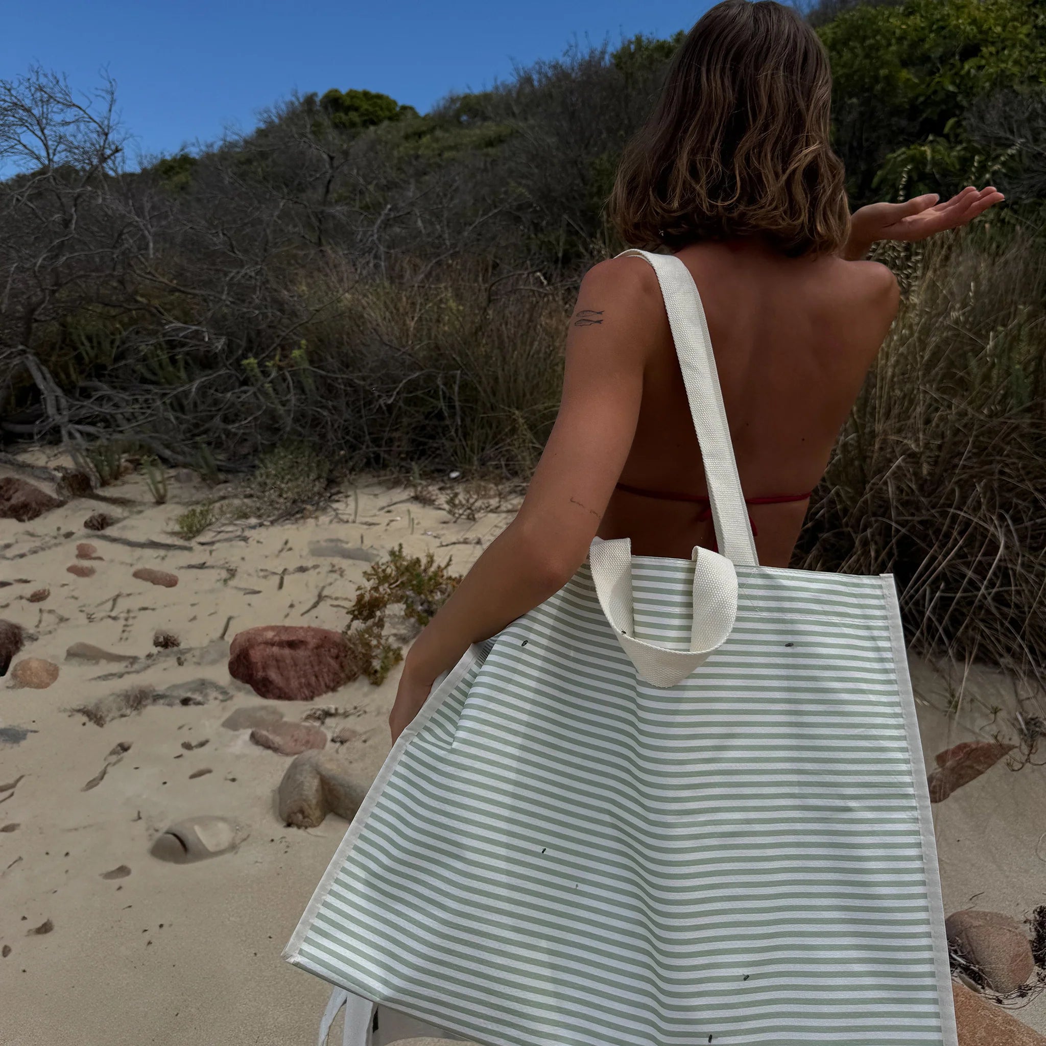 Torba plażowa pasiasta marki LOQI na ramieniu kobiety na piaskowej plaży
