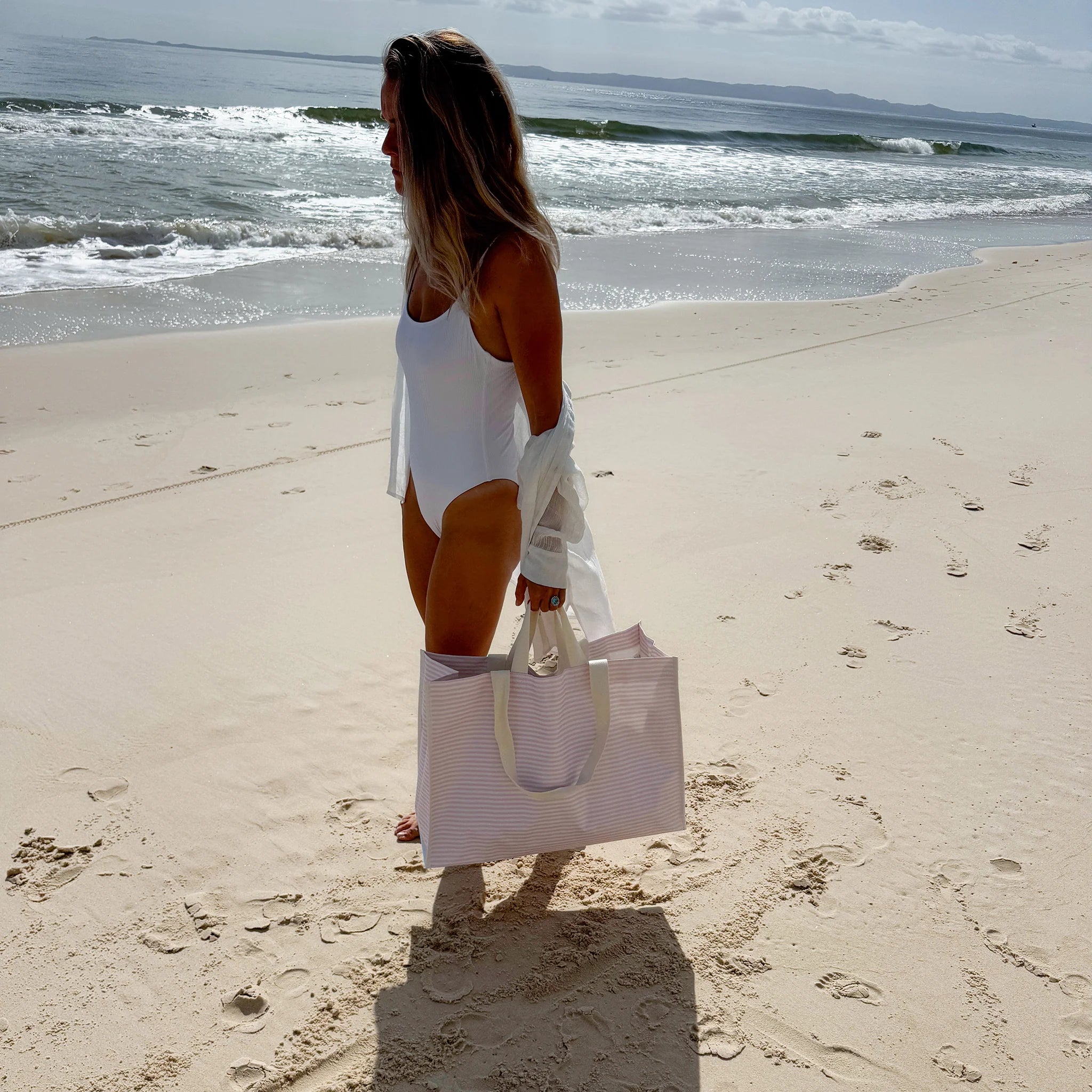 Kobieta na plaży trzymająca torba plażowa różowa od LOQI z paskami na ramię