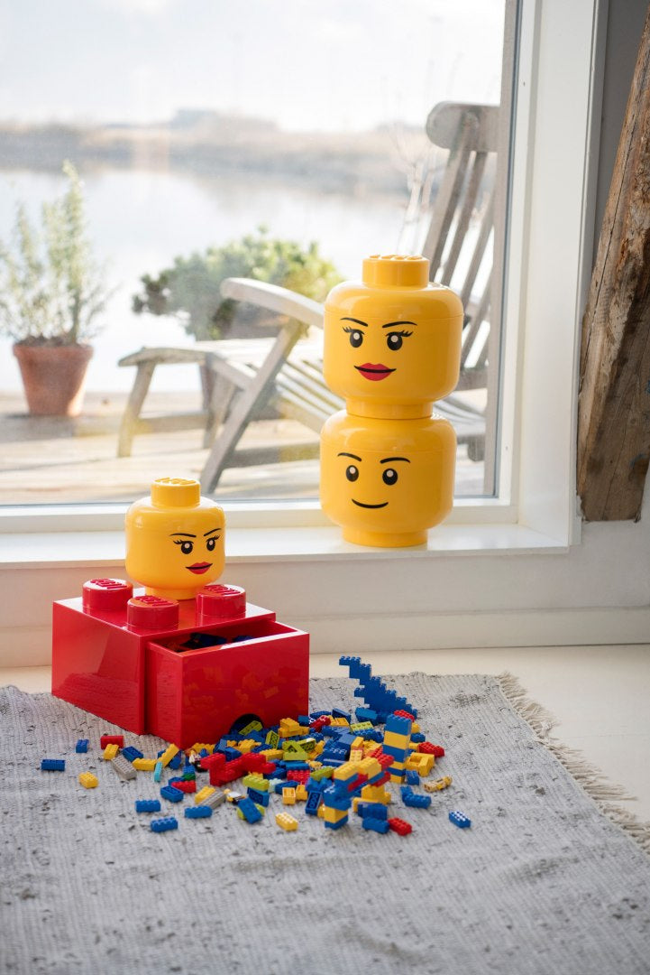 Czerwona szuflada LEGO Brick 4 z dwoma żółtymi głowami klocków na szarym dywanie przy oknie