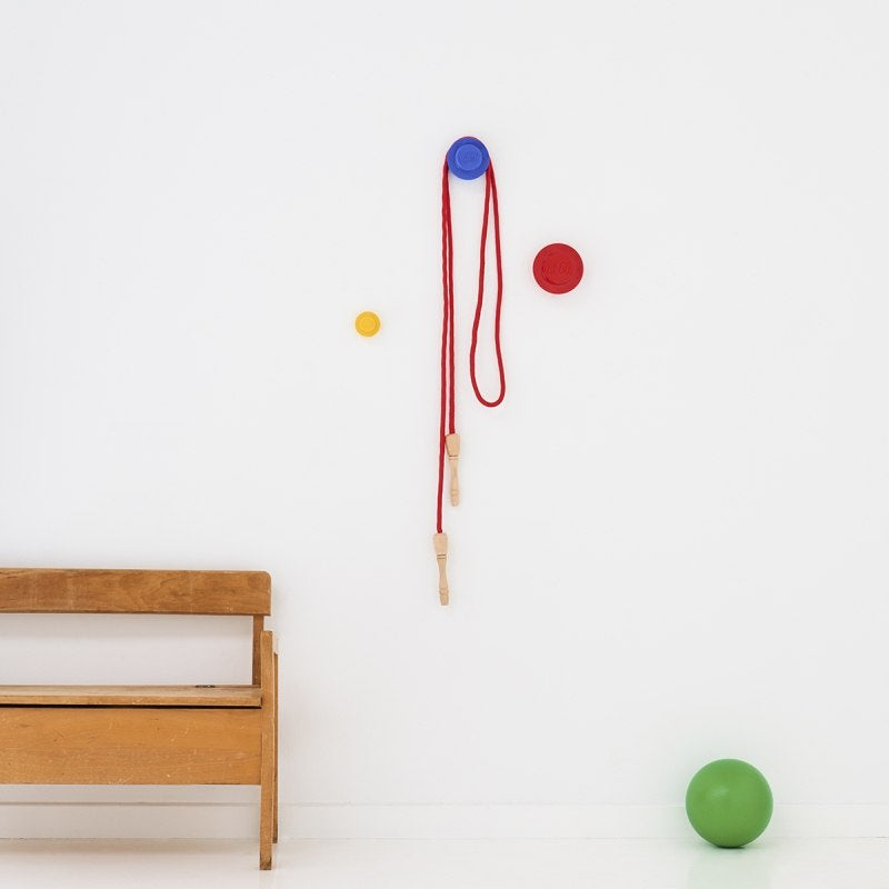 Kolorowe wieszaki LEGO na ścianę zamontowane na białej ścianie nad drewnianą ławką w pokoju