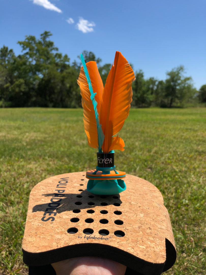 Lotka Waboba Flyer z pomarańczowymi piórami na desce do gry w volan na tle zielonej trawy