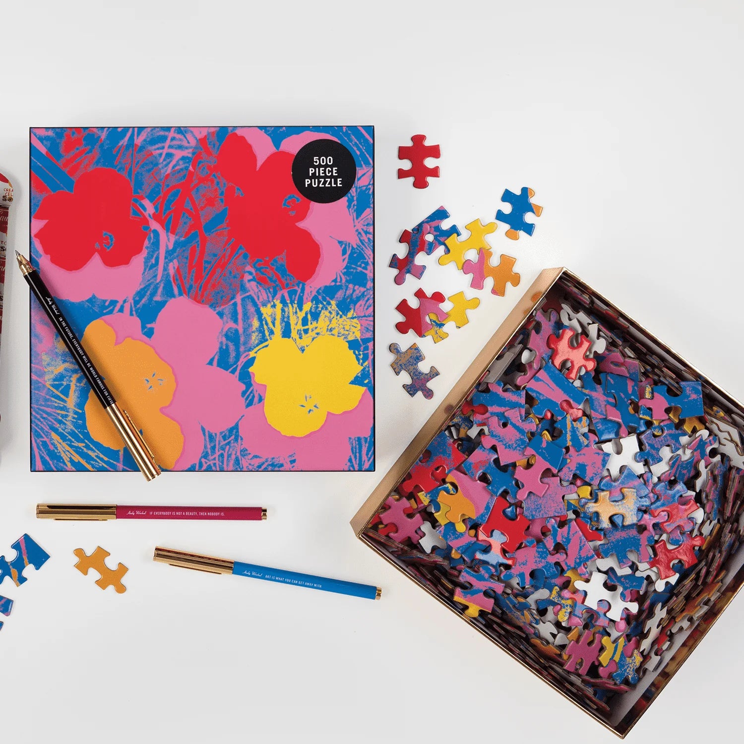 Puzzle Andy Warhol Flowers 500 elementów z kolorowymi kwiatami i rozrzuconymi elementami obok pudełka