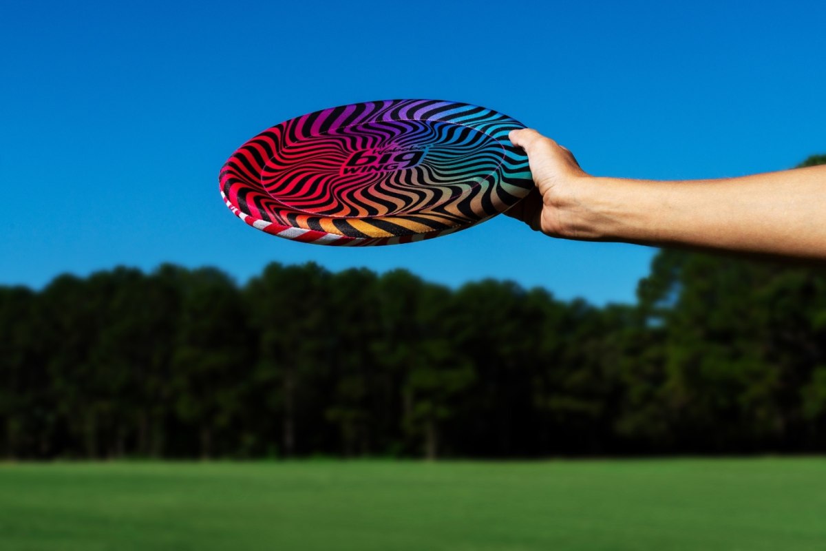 Kolorowy latający dysk Waboba Bigwing trzymany w dłoni na tle nieba i zielonej trawy