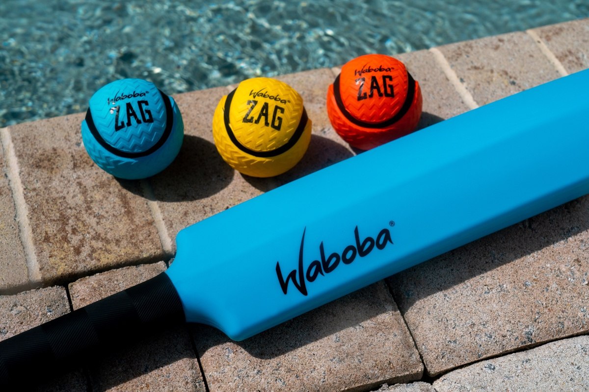 Kolorowe piłeczki Waboba ZAG obok niebieskiej pałki do gry nad basenem