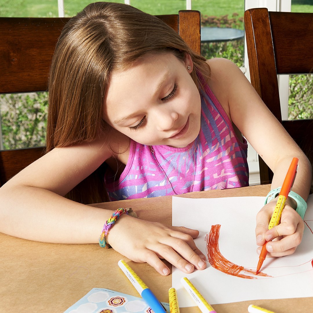 Dziewczynka malująca rysunek flamastrami zapachowymi Chupa Chups przy drewnianym stole