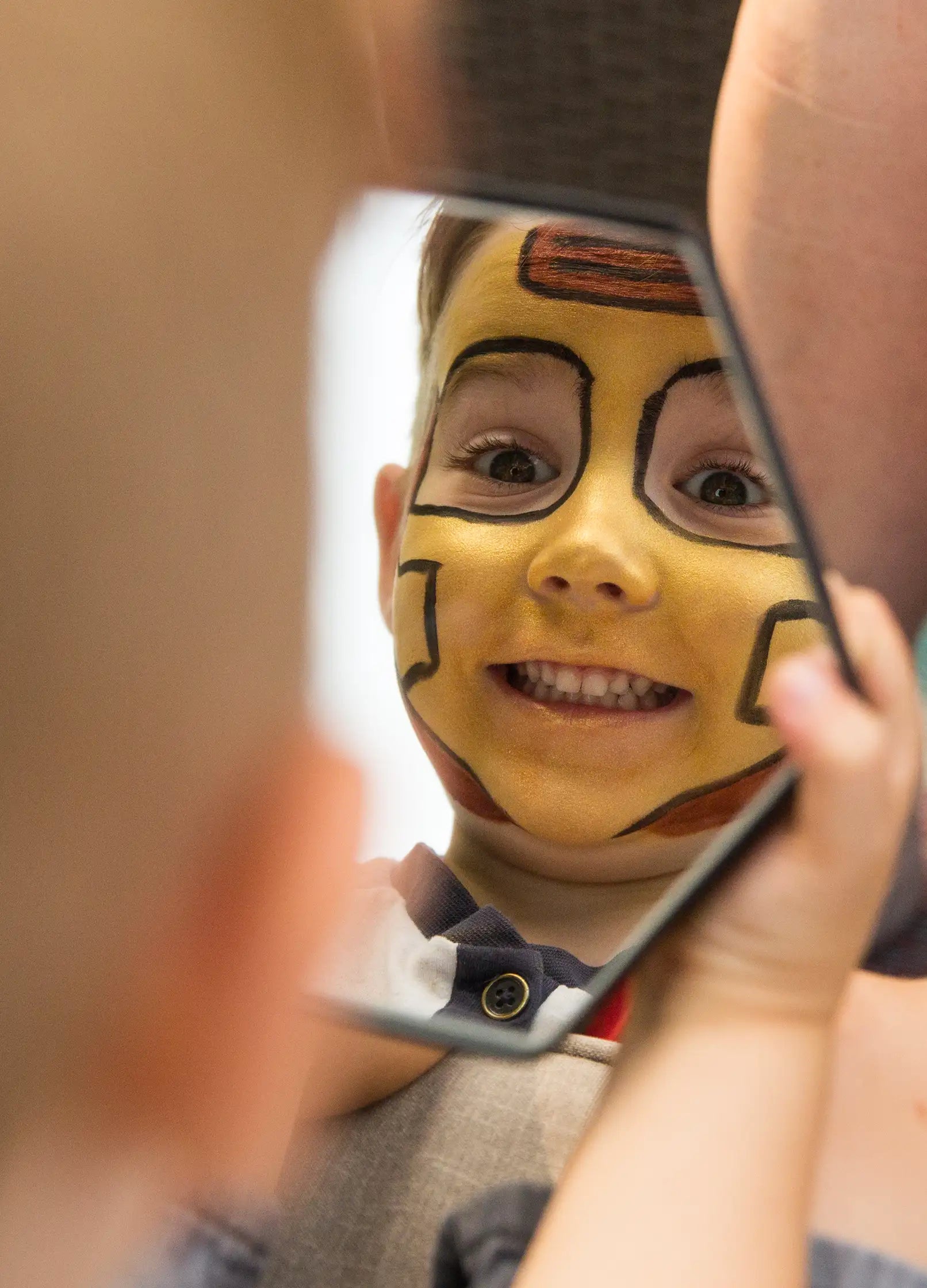 Dziecko z twarzą pomalowaną w żółto-czarne wzory patrzy w lustro zestawu do malowania twarzy dla dzieci